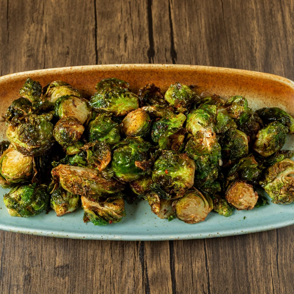 A light blue and brown platter filled with roasted Brussels sprouts on a wooden table.