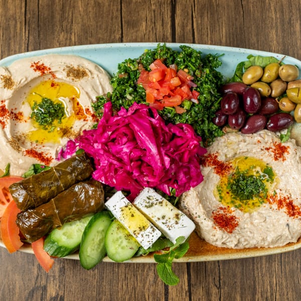 A large platter of Mediterranean appetizers, including hummus, tabbouleh, stuffed grape leaves, and olives.
