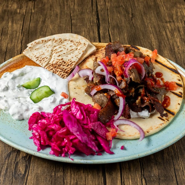 Mediterranean gyro plate with meat, red onions, tomatoes, tzatziki, pickled cabbage, and pita bread.