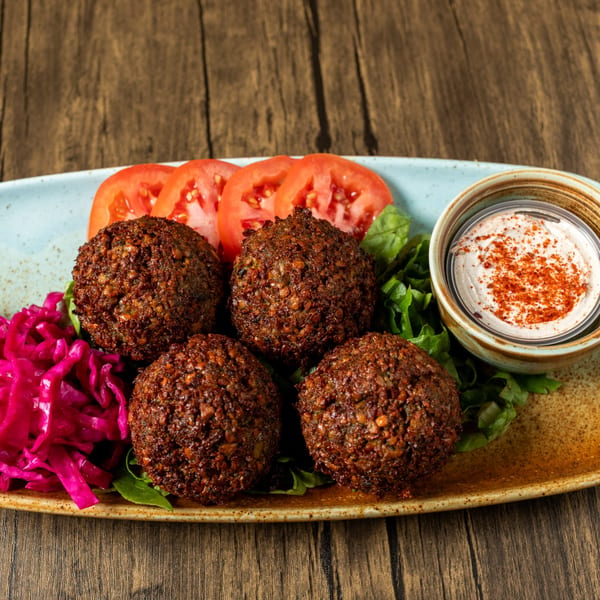 Four falafel balls on a bed of lettuce with sliced tomatoes, pickled cabbage, and a dip.