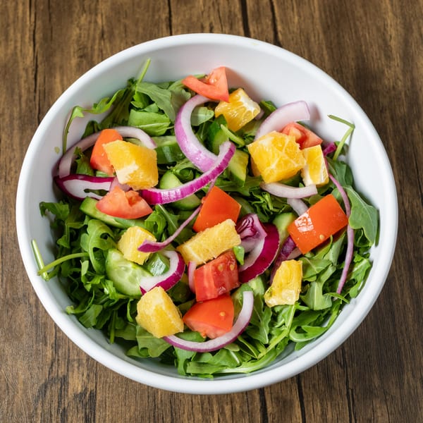 A fresh Mediterranean salad with arugula, tomatoes, red onion, cucumber, and orange segments.