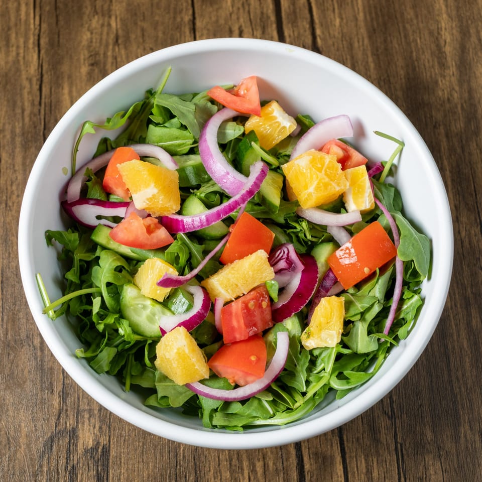 A fresh Mediterranean salad with arugula, tomatoes, red onion, cucumber, and orange segments.