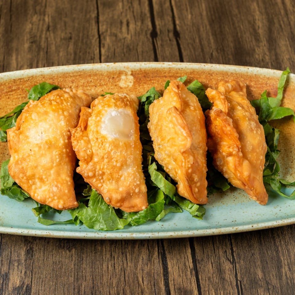 Four golden-brown fried pastries, likely Mediterranean empanadas, served on a bed of fresh green lettuce.