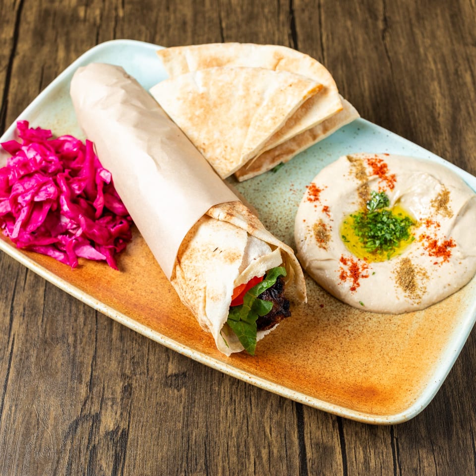 Mediterranean shawarma wrap, hummus, pita bread, and pickled cabbage on a rustic wooden table.