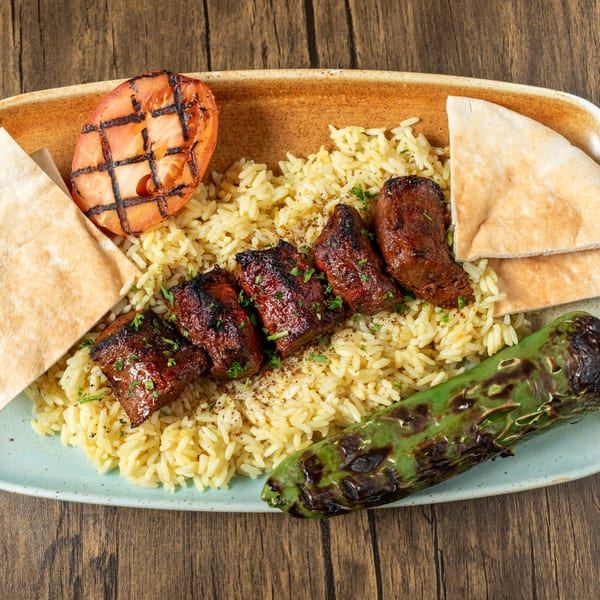 Mediterranean shish kebab with rice, grilled tomato, charred green pepper, and pita bread on a plate.