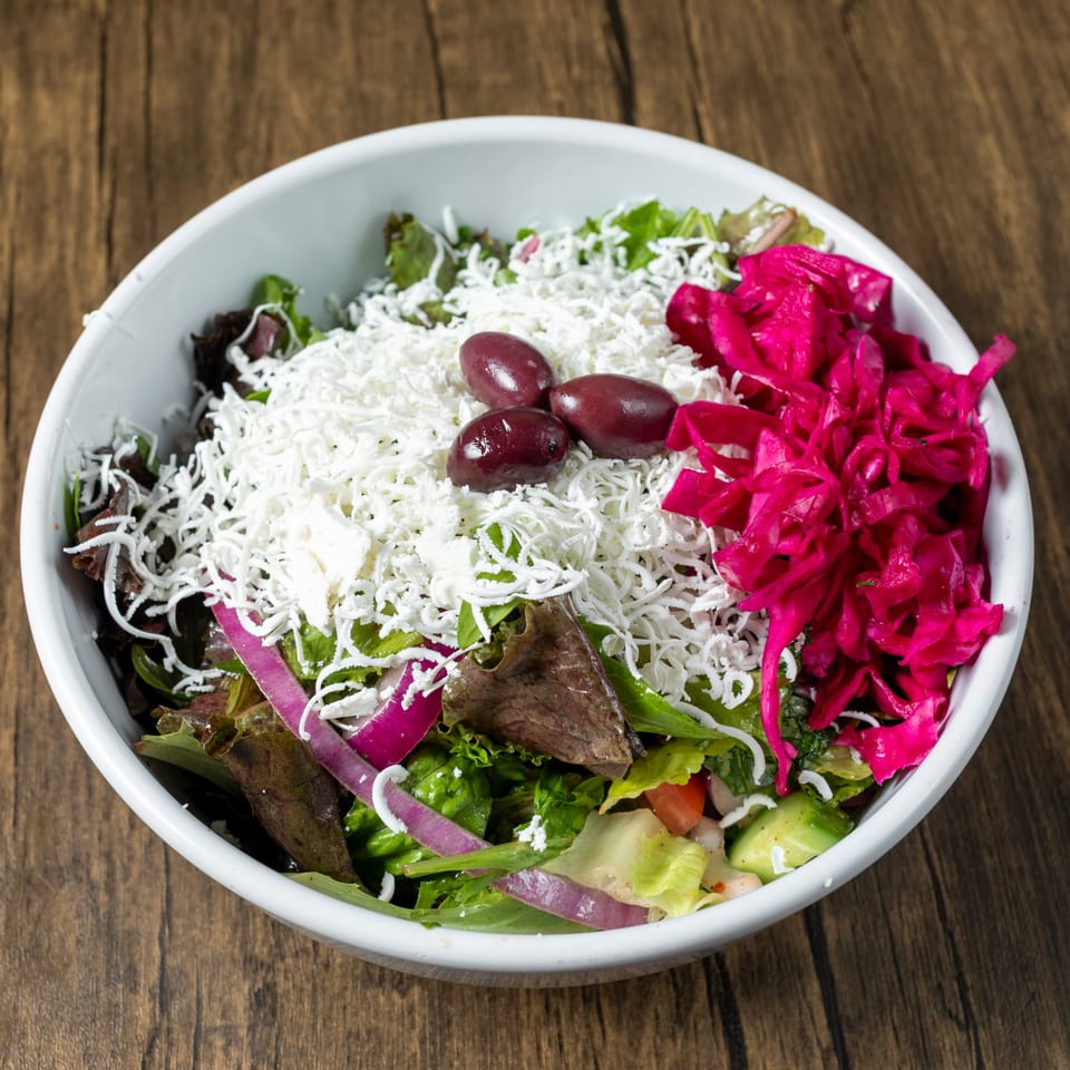 Mediterranean salad with mixed greens, feta cheese, olives, red onions, and pickled cabbage in a white bowl.