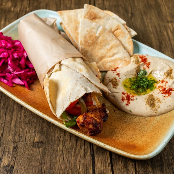 Mediterranean chicken shawarma wrap, hummus, pita bread, and pickled cabbage on a rustic plate.