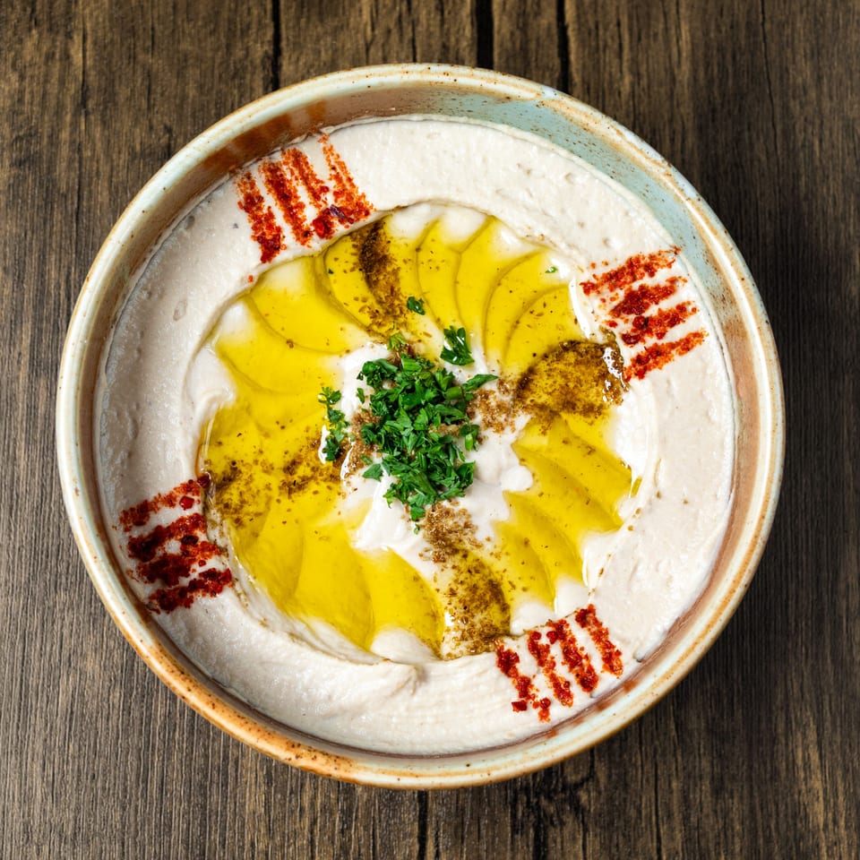 A bowl of creamy hummus, drizzled with olive oil, sprinkled with paprika, za'atar, and fresh parsley.